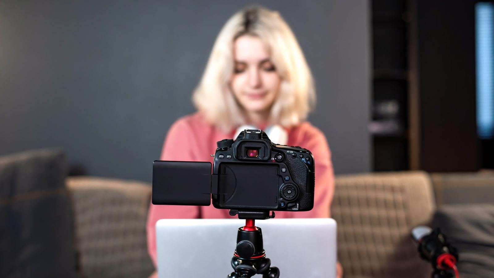 A creator filming herself at home with a camera on a tripod and a laptop on the table.