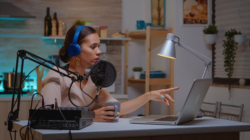 A live broadcast host speaking into a microphone wearing headphones in a home studio.