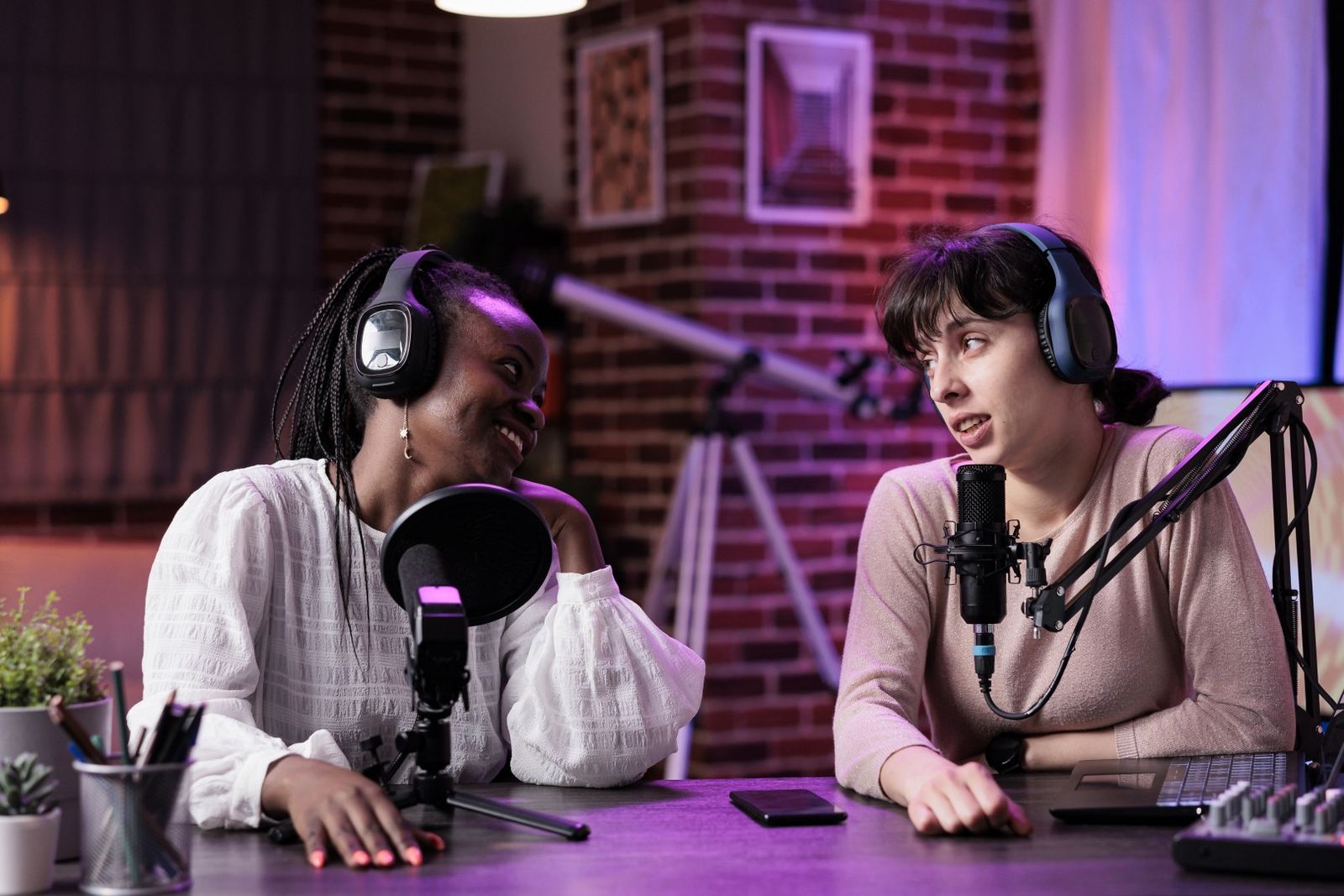 Two podcast co-hosts recording an episode together at microphones in a neon-lit studio.